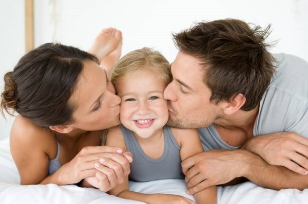 Father and mother kissing daughter