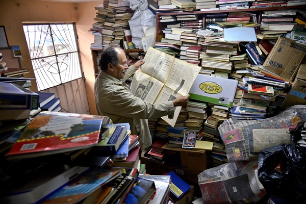 Jose Alberto Gutierrez reads an old newspaper among books stacked in his library on the first floor of his house in Bogota, on May 18, 2017.  Bogota has who rescues its books. For more than two decades Jose Alberto Gutierrez - "The Lord of Books", as he is known in Colombia - drives a garbage truck through the gray and cold streets of Bogota. In addition to wastes, he has collected thousands of books that crowded into his home, converted into a free library. / AFP PHOTO / GUILLERMO LEGARIA COLOMBIA-SOCIETY-BOOKS-RESCUER