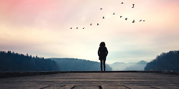 Woman standing on jetty and watching sunrise by the lake.